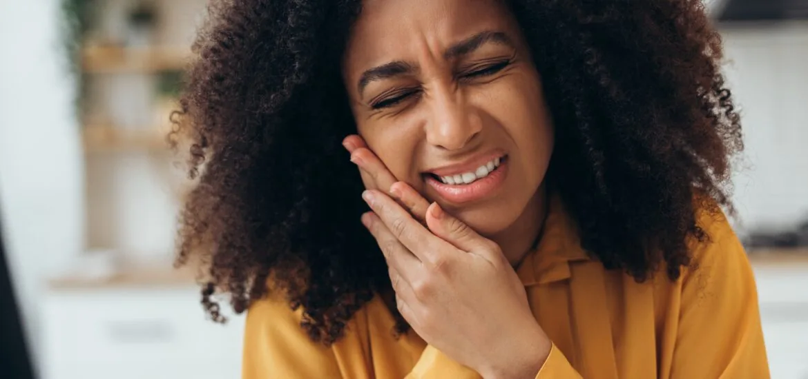 closeup of a young woman holding her jaw, indicating serious tooth pain