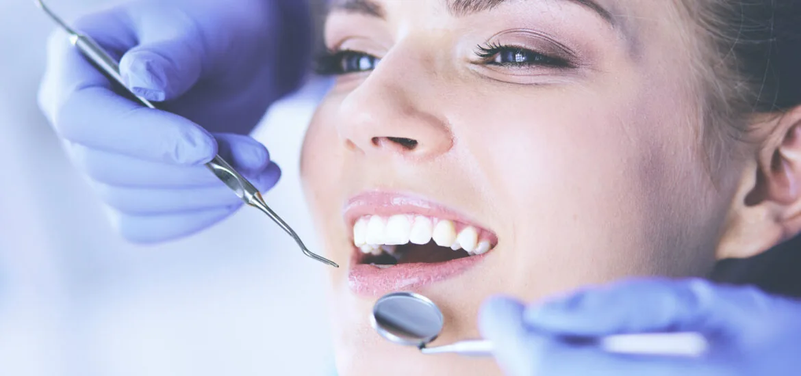 closeup of a dentist in blue gloves checking a woman's teeth for cavities