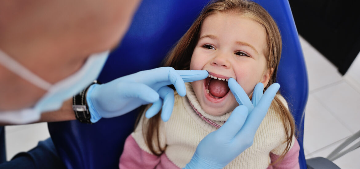 Male dentist in sterile medical mask examining baby teeth