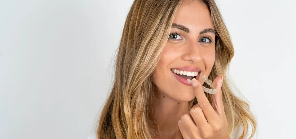 young woman placing her clear aligners in her mouth against a white backdrop