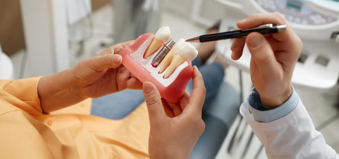 A close-up of an unrecognizable old woman with a dentist showing her an implant model