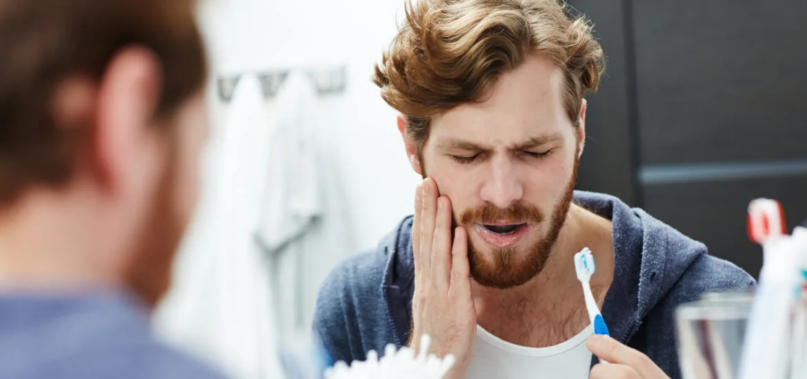 young man brushing his teeth in mirror, sensitive tooth, tooth infection